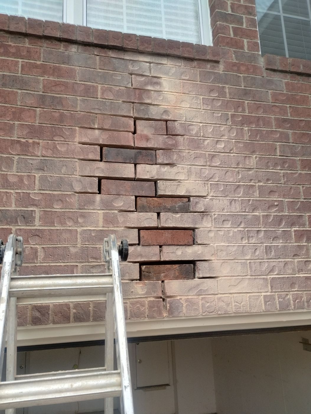 Brick Wall Crack and Lintel Repair Vertical and horizontal cracks are visible in the brick wall above a garage door
