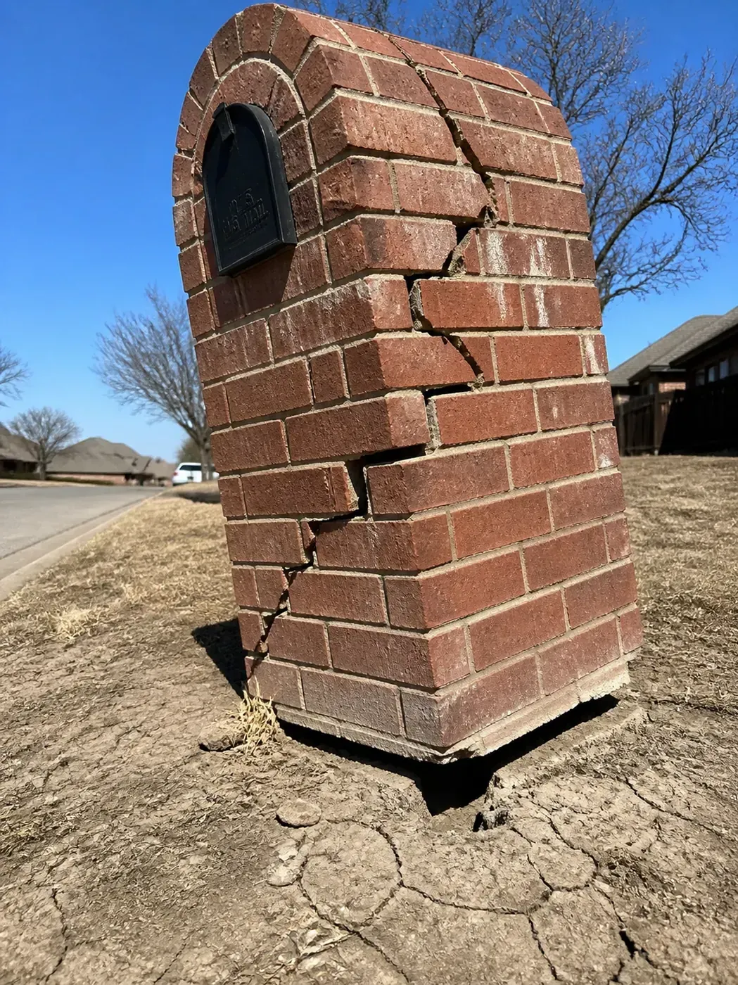 Leaning brick mailbox in Dallas with stair-step cracks caused by soil foundation failure.