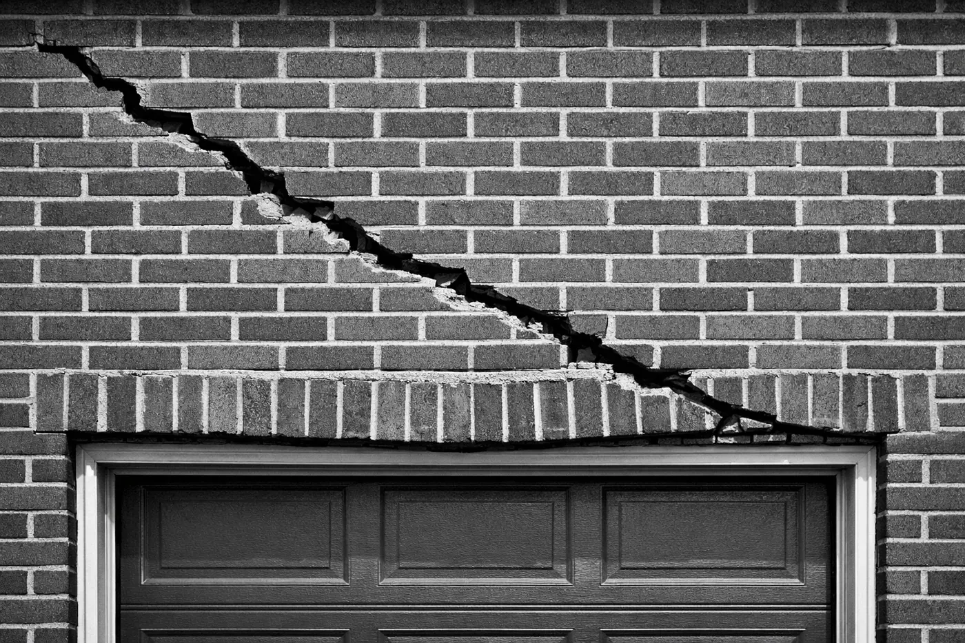 Diagonal crack in brick wall above garage door showing lintel failure and structural damage