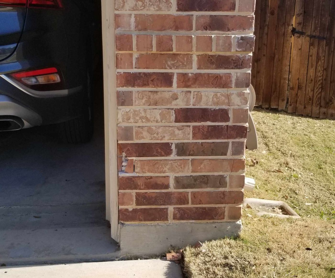 Damage to a brick garage wall corner that requires structural assessment and matching brick replacement.